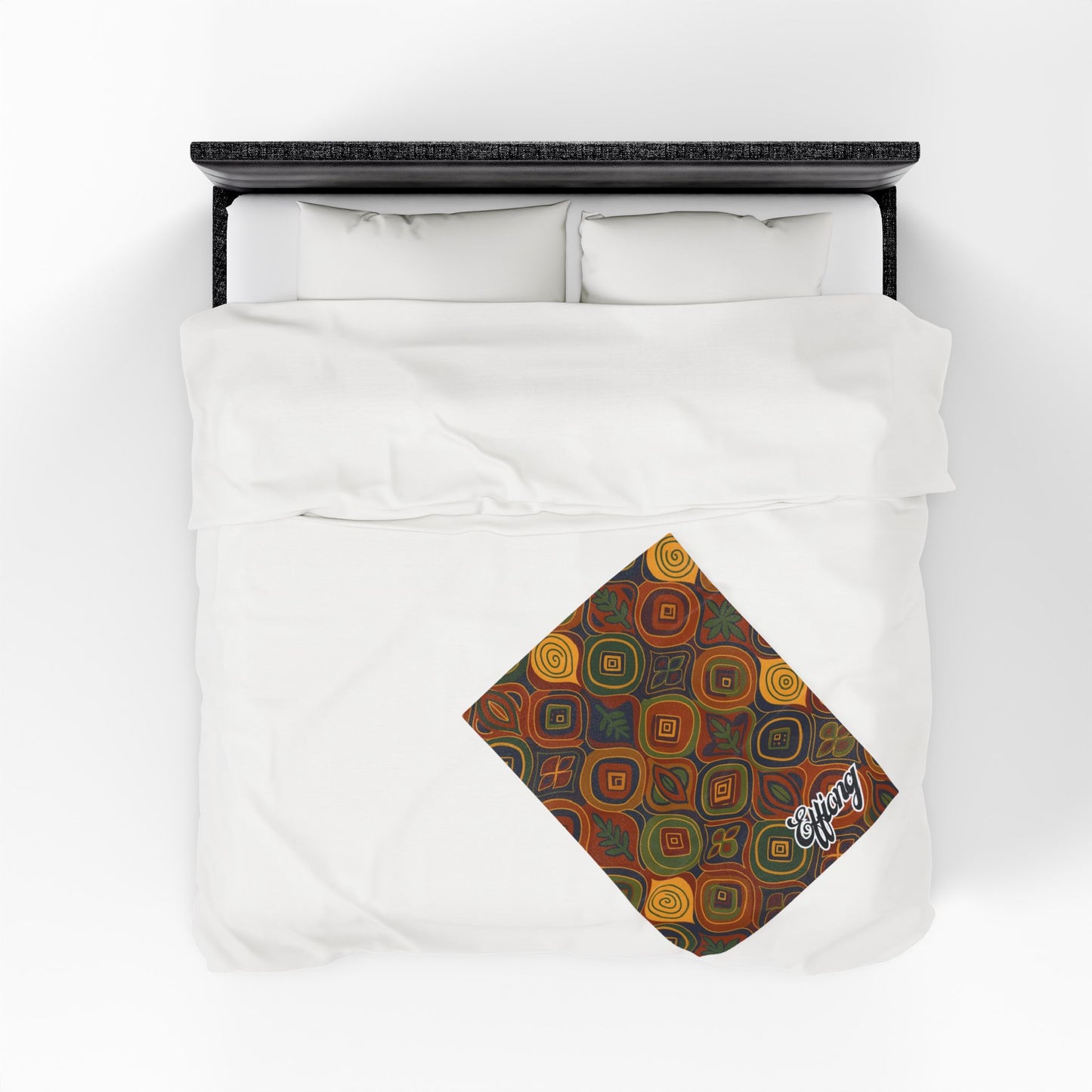 A neatly made bed with white bedding viewed from above. An African-inspired blanket with a colorful geometric pattern is folded at the foot, featuring the word coffee in white script—perfect as a custom gift or personalized velveteen blanket.