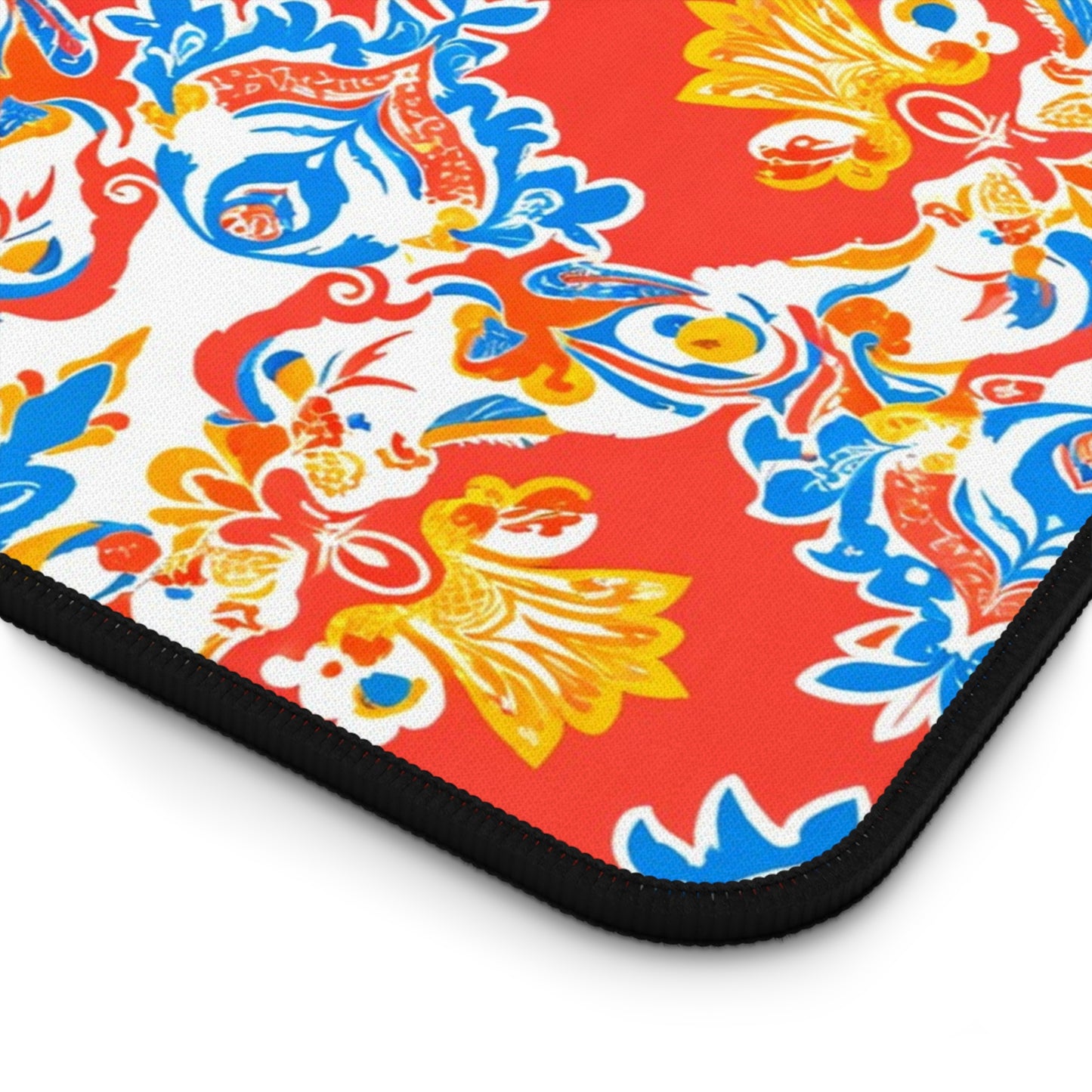 A close-up of a Neoprene desk mat with a vibrant, ornate floral pattern. Swirling yellow, blue, and white flowers and leaves adorn the red background, while the black textured edge offers a glimpse of this stylish workspace accessory.