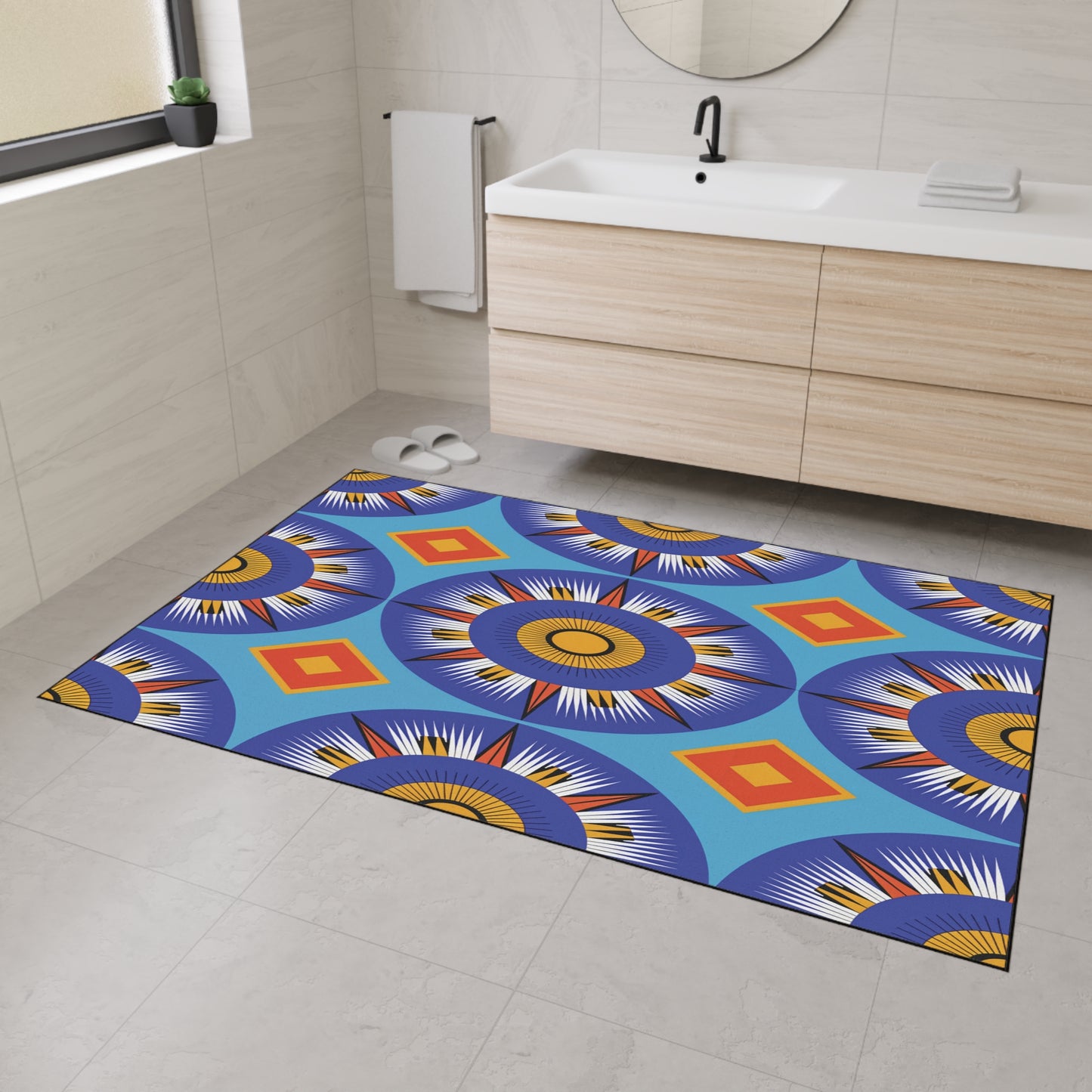A modern bathroom with light beige tile floors and walls features an African-inspired rectangular rug with bold geometric and circular patterns in blue, orange, yellow, and white. The custom floor mat has a non-slip rubber backing for safety near the wooden vanity.