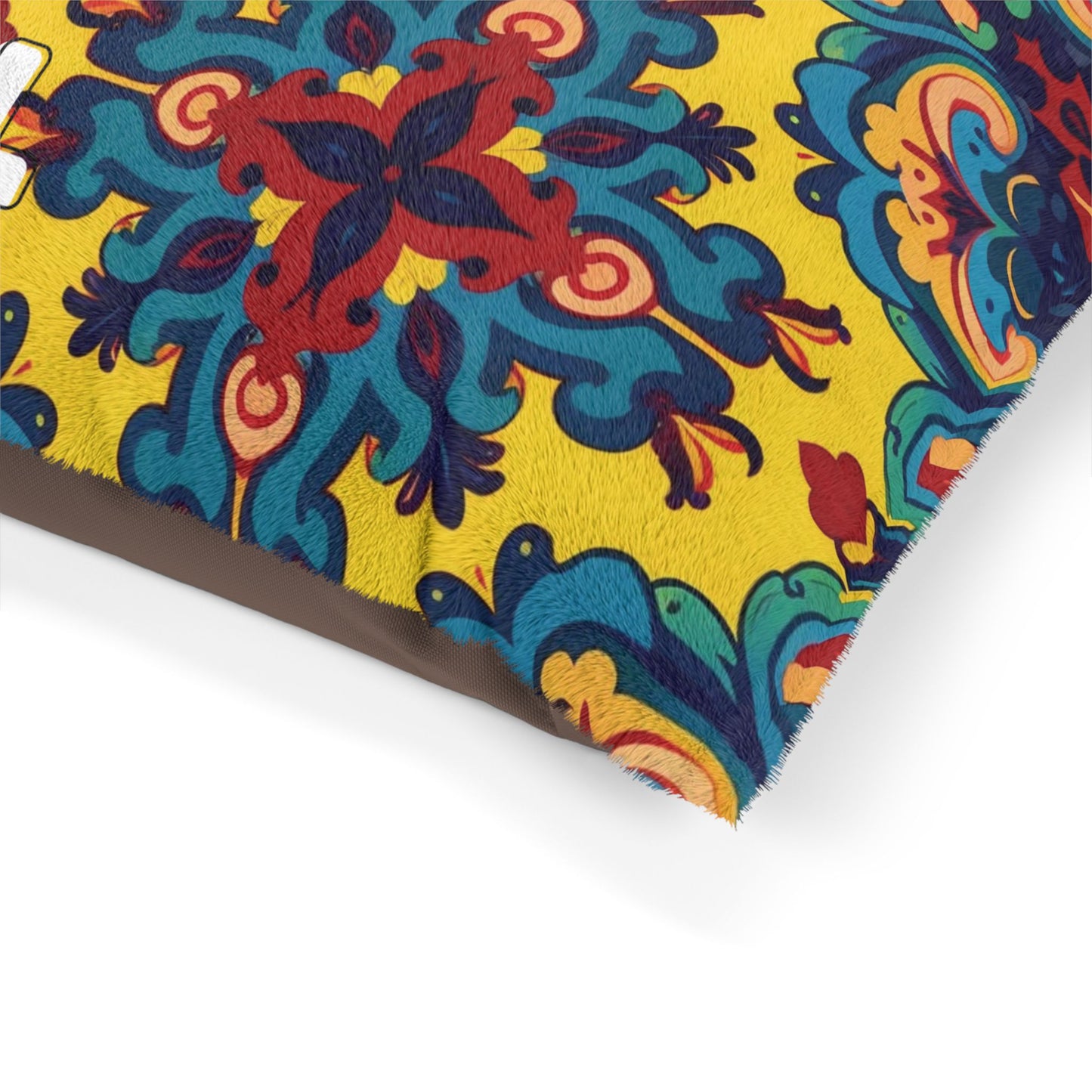 A close-up of a stylish pet pillow with a vibrant pattern. The design showcases intricate blue, red, and orange floral motifs on a bright yellow background. Fine white stitching details the edges, and the fabric appears soft with a slight sheen.