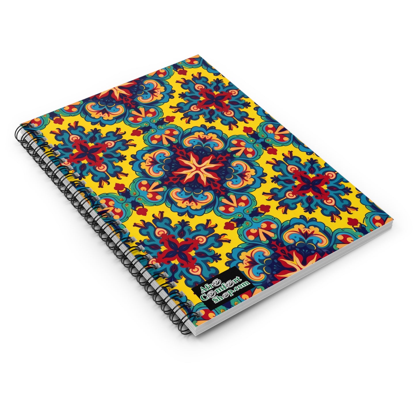 A spiral-bound, African-inspired spiral notebook lies closed, featuring a vibrant yellow cover with bold, symmetrical red, blue, and orange floral patterns reminiscent of traditional tile designs. The lower right corner displays a small “Good Vibes Inspiration” label.