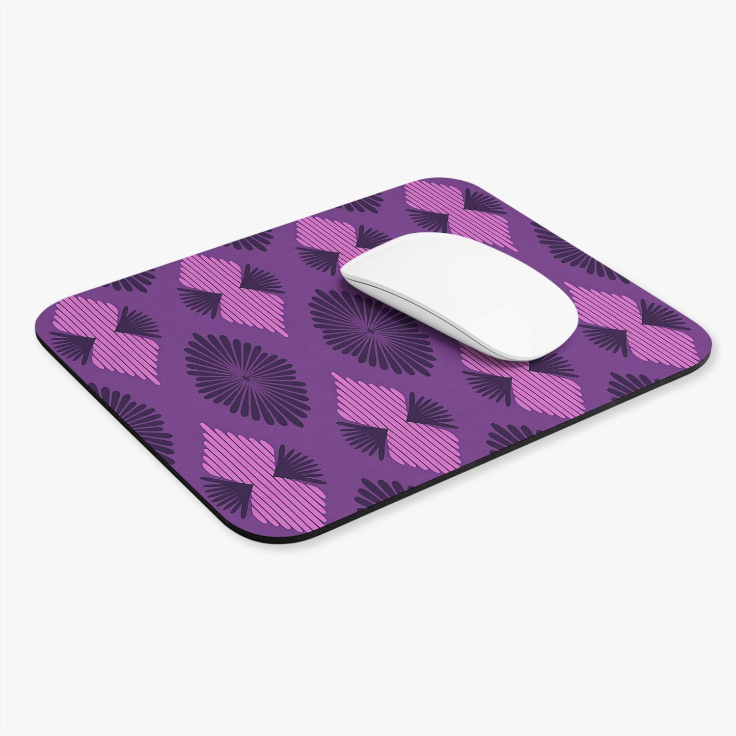 A rectangular African-inspired mouse pad with rounded corners features a purple background and abstract, fan-shaped black and pink designs. A white wireless computer mouse rests on its smooth surface, which includes a non-slip rubber base for stability.