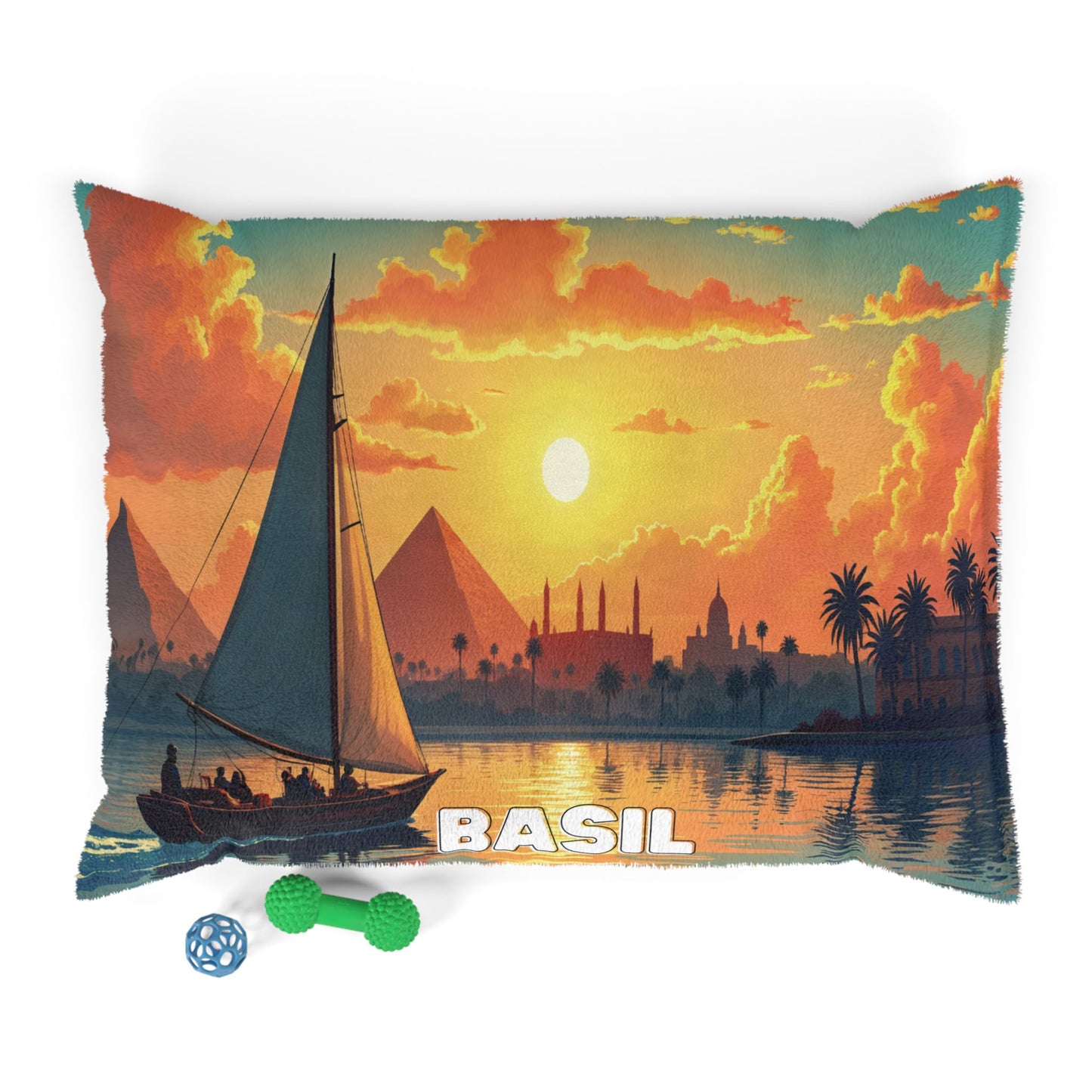 A rectangular pillow with durable construction features a vivid sailboat scene at sunset, pyramids, palm trees, and a mosque silhouette. “BASIL” is printed at the bottom. Two dog toys rest nearby, perfect for personalized pet beds.