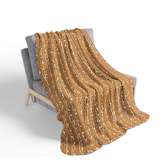 A soft gray chair with wooden legs is draped with a thick, knitted blanket. African-inspired fleece blankets in warm brown with white and blue accents add a cozy home decor touch, creating texture against the plain white background.