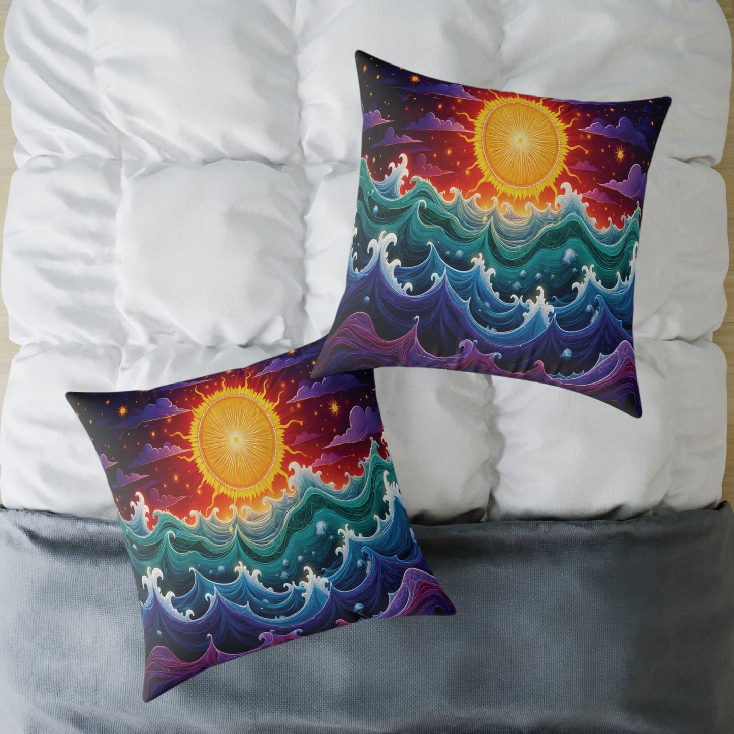 Two vibrant accent pillows rest on a white, tufted comforter and gray blanket. Each pillow features bold, glowing sun art above swirling waves, creating colorful home decor with a dreamy, seascape-inspired design.