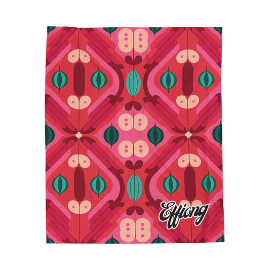 A vibrant, African-inspired blanket features a bold geometric pattern in red, pink, teal, and beige. “Effiong” is written in white script on the lower right corner. This personalized velveteen blanket has a retro, mid-century modern feel.