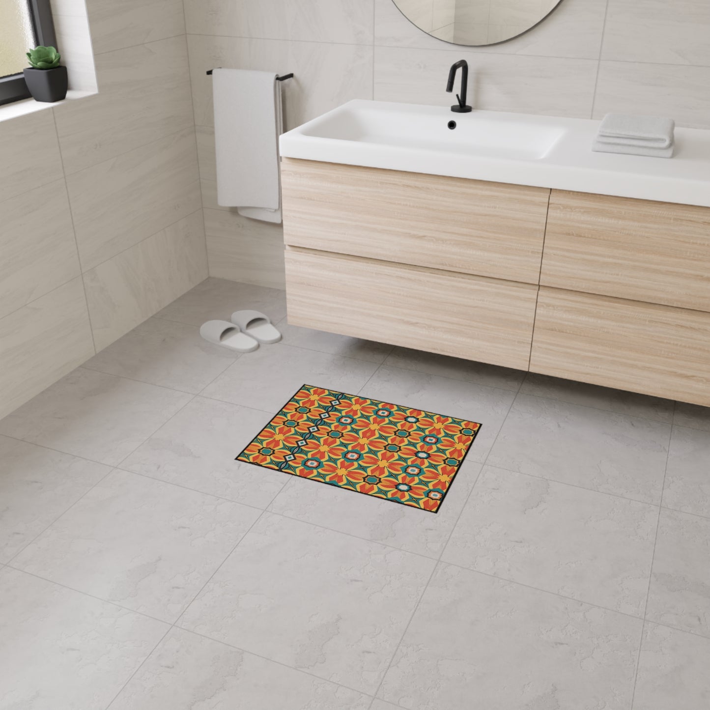 A modern bathroom with light gray tiled floor and walls, a floating wood vanity with a white sink, a round mirror, white towel, and slippers. An African-inspired floor mat with an orange, green, and black geometric pattern adds color.