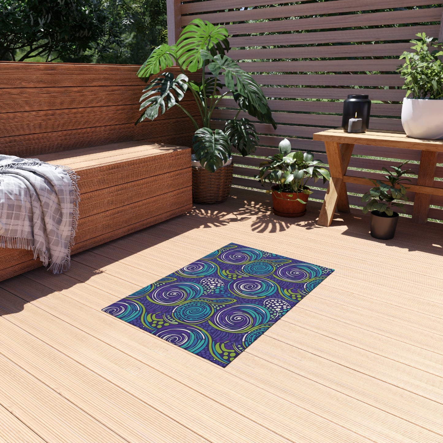 A cozy wooden deck with a built-in bench draped in a gray blanket, potted green plants, a small wood table with a black teapot and cup, and an African-inspired outdoor rug with swirling blue, purple, and green patterns. Sunlight creates a warm atmosphere.