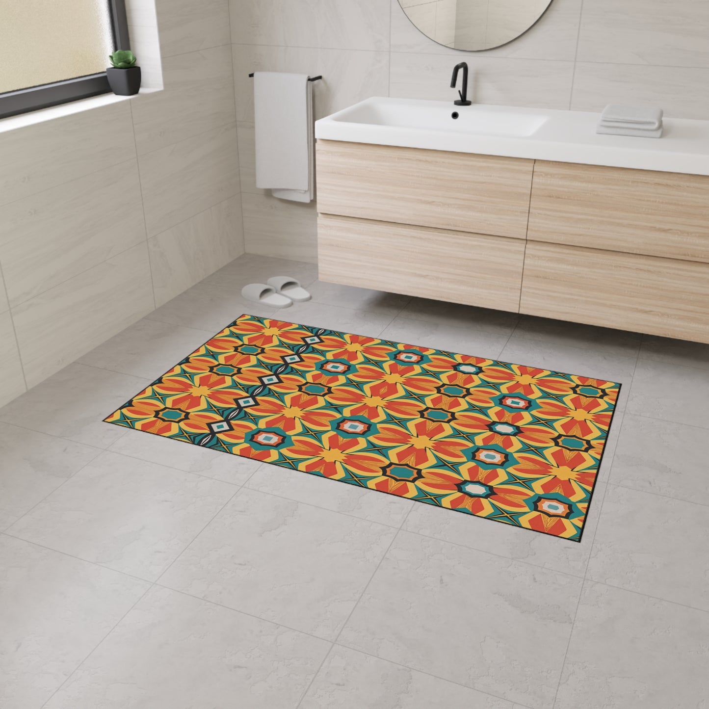 A modern bathroom with light gray tile floors and walls, a floating wood vanity with a white sink, and a round mirror. The vibrant custom floor mat features an orange, yellow, and green geometric floral pattern with non-slip rubber backing.