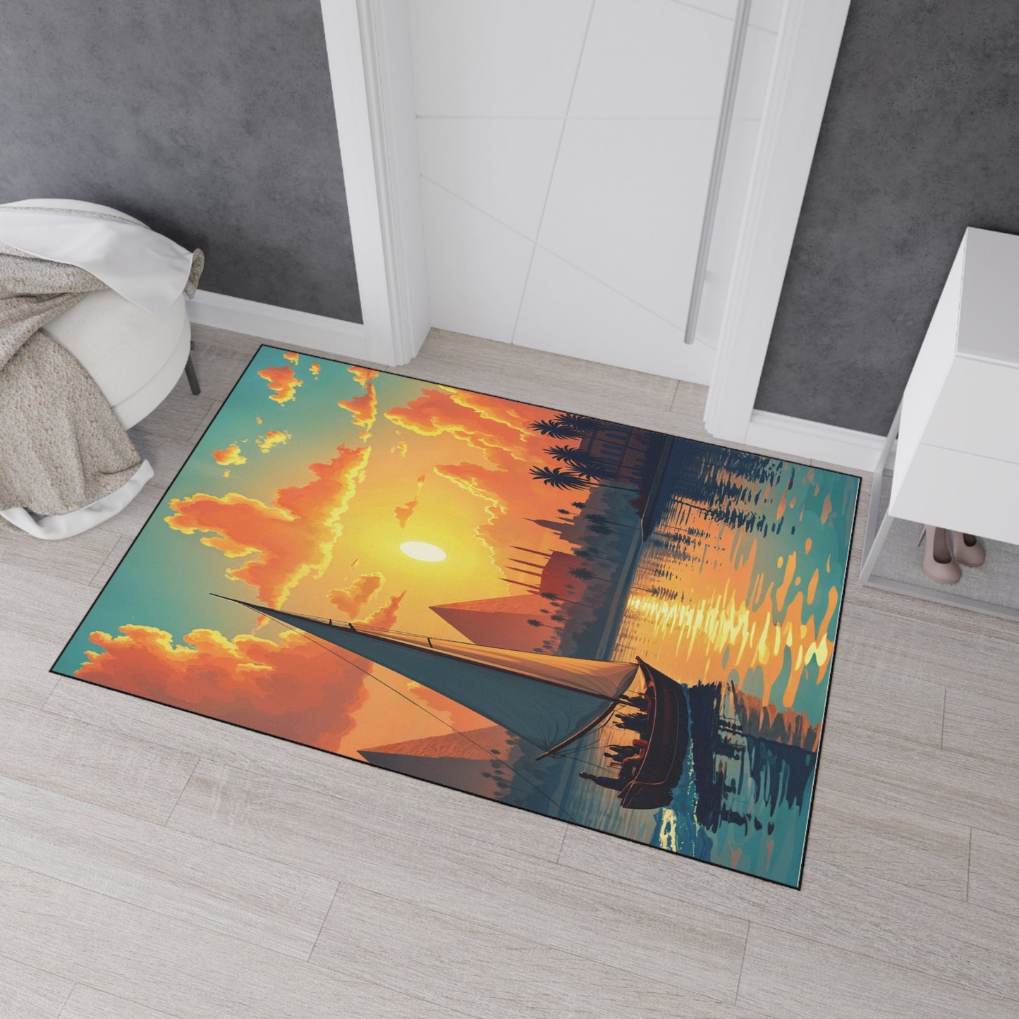 A colorful rectangular rug with non-slip rubber backing on a light wood floor features a vivid sunset scene with a sailboat, palm trees, and birds. The bright sky glows orange and yellow near a white cabinet, closed doors, and a beige blanket.