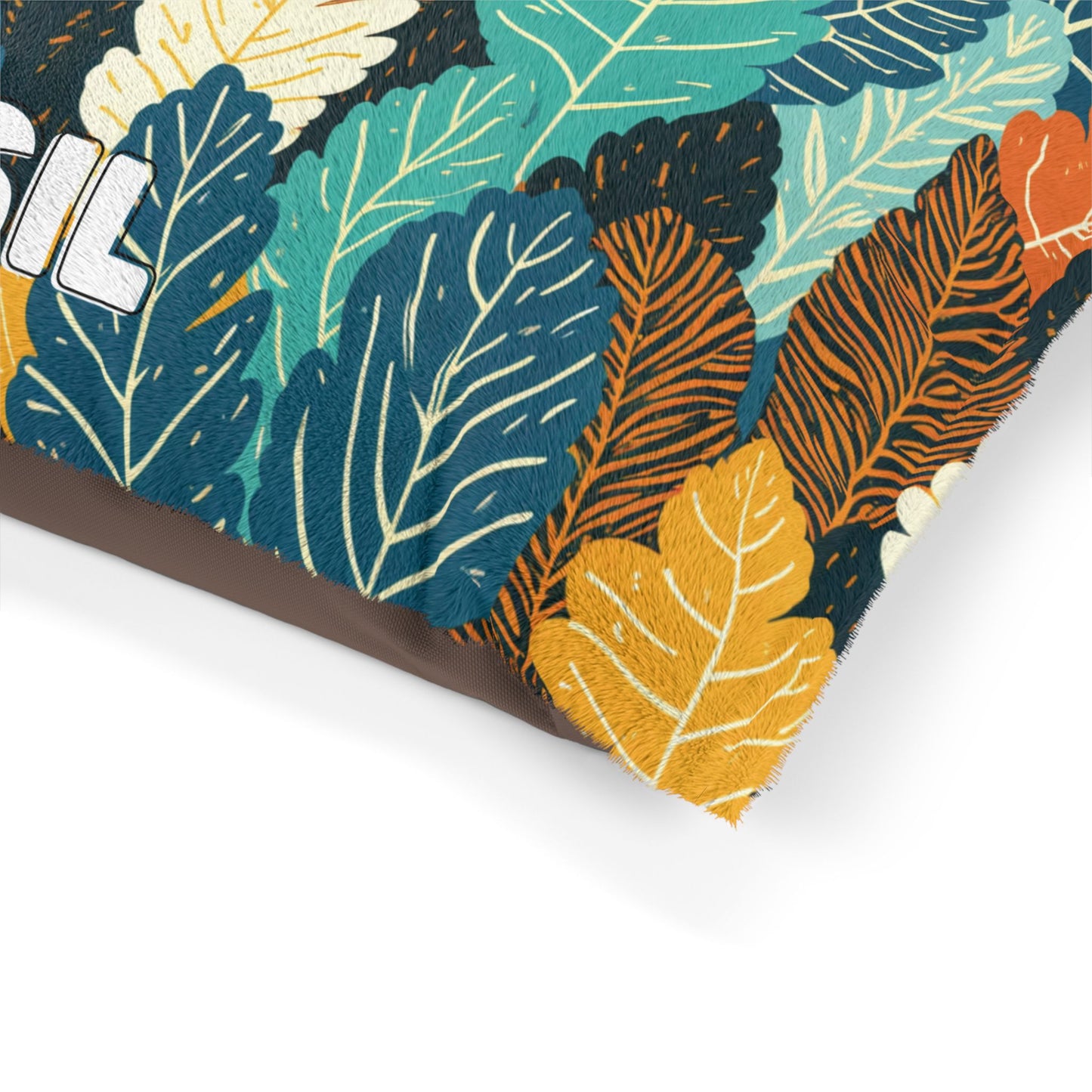 A close-up of a fabric cushion with a vibrant leaf pattern in teal, yellow, orange, white, and blue. The leaves are illustrated in various shapes and overlapping layers, showcasing durable construction. The edge of the pillow and partial word “SOIL” are visible on the left.