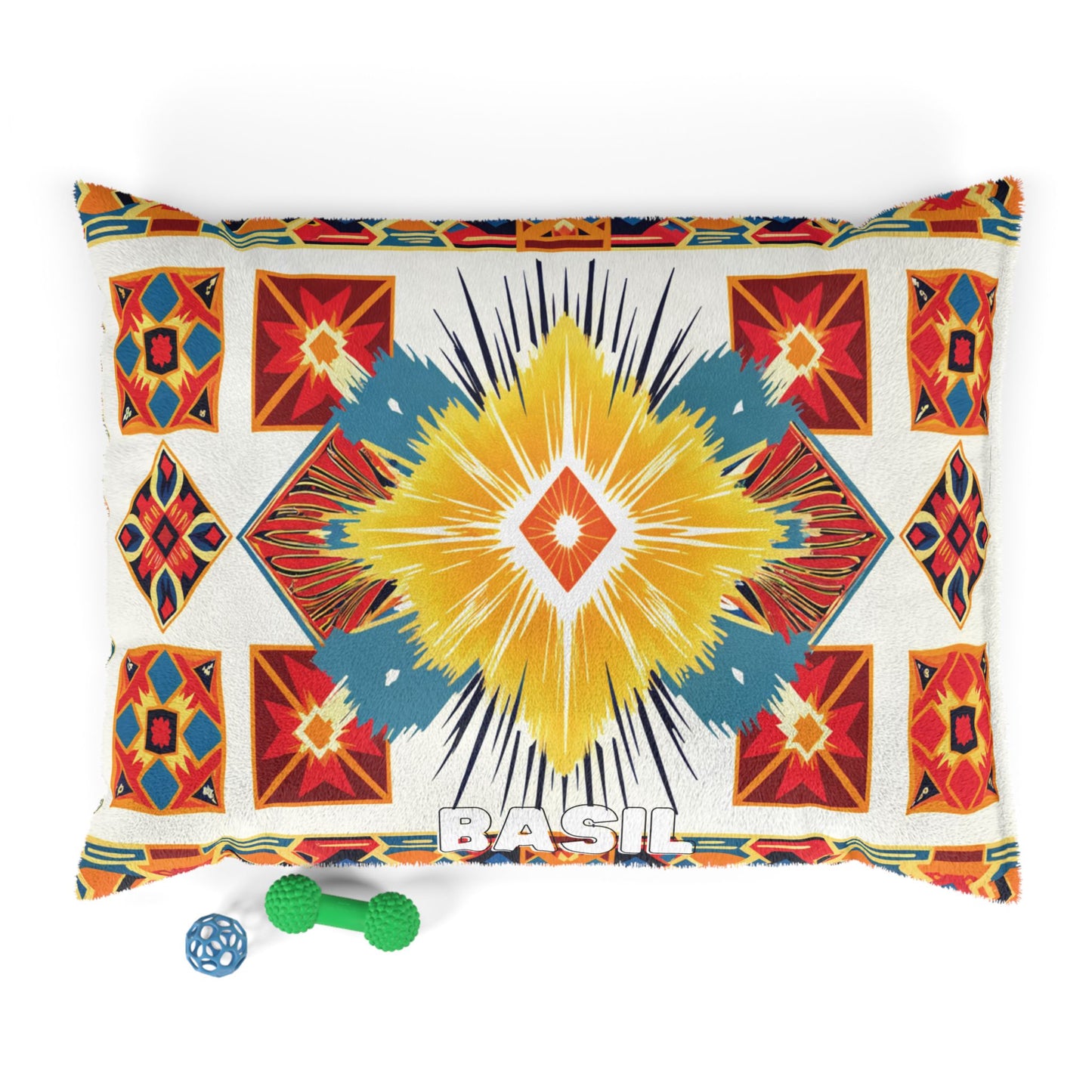 A rectangular pillow with a colorful geometric southwestern and African-inspired pattern in yellow, blue, red, and orange, featuring the name “BASIL” at the bottom center. Two dog toys—a blue ball and a green textured bone—sit by the lower left corner.