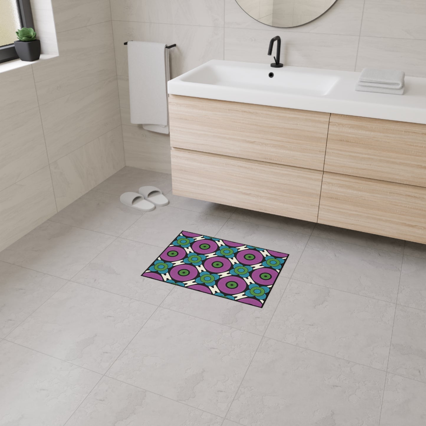 A modern bathroom with light wood vanity, white sink, round mirror, towel, and slippers. On the gray tile floor is a colorful geometric mat featuring African-inspired aesthetics and non-slip rubber backing for added safety.