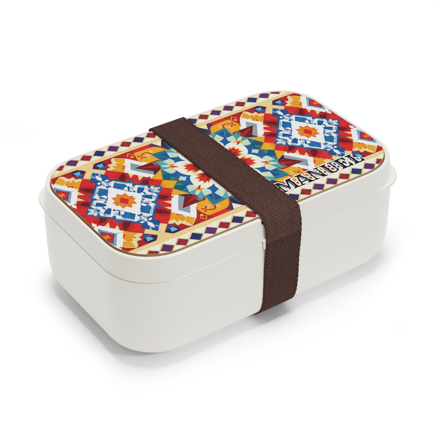 A BPA-free, personalized lunch box with a colorful, geometric, and floral patterned lid in red, blue, yellow, and orange tones. Inspired by African bento lunch boxes, “MANUEL” is printed on the lid and a wide dark brown elastic band keeps it secure.
