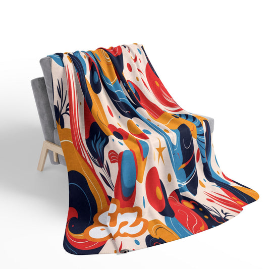 A modern chair is draped with an African-inspired fleece blanket featuring an abstract, playful pattern in red, orange, blue, yellow, black, and white shapes. The white background highlights the vibrant sherpa fleece design.