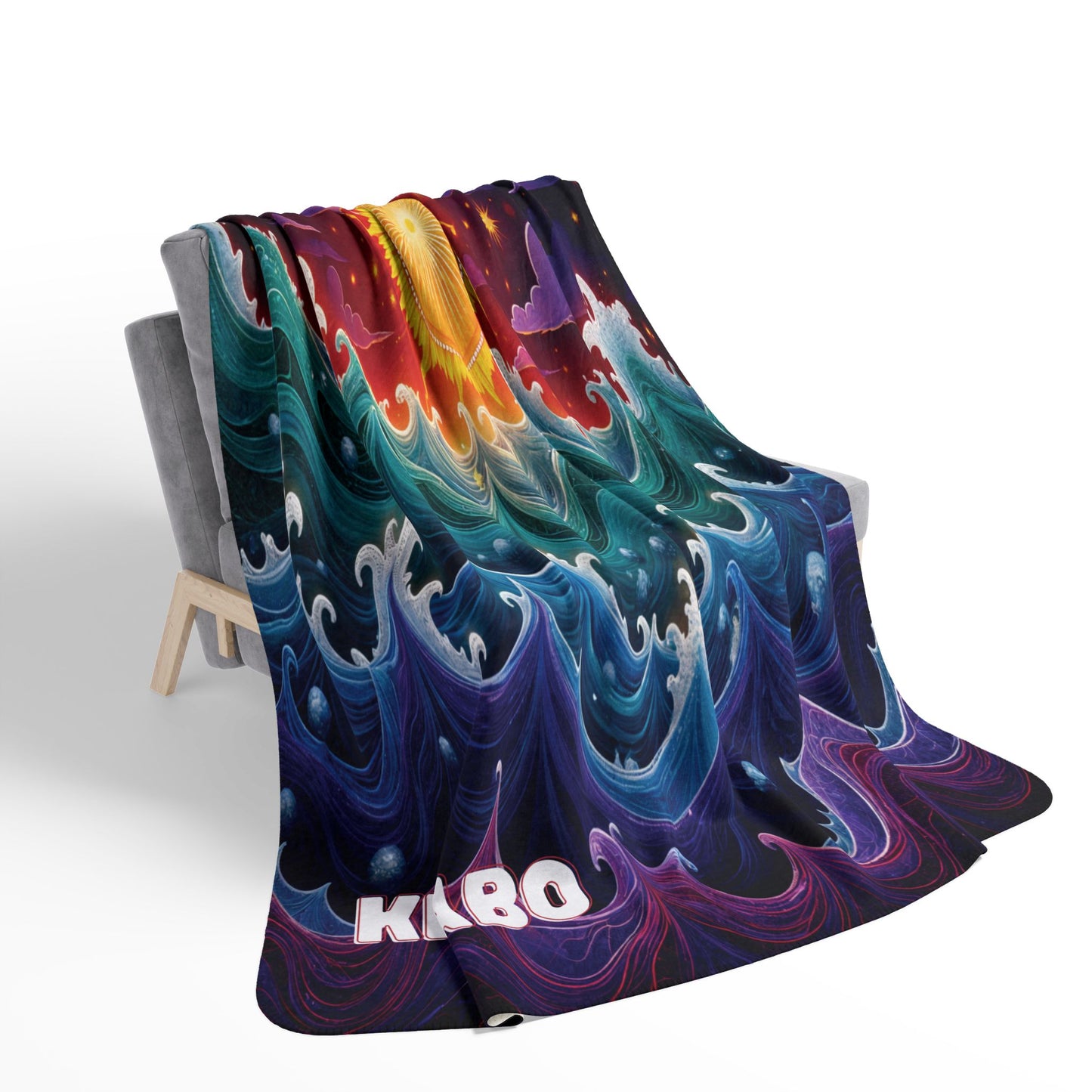 A colorful, African-inspired blanket draped over a modern gray chair features swirling wave patterns in blue, purple, green, yellow, and red hues. The letters KABO appear in bold white and pink near the bottom edge of the blanket.