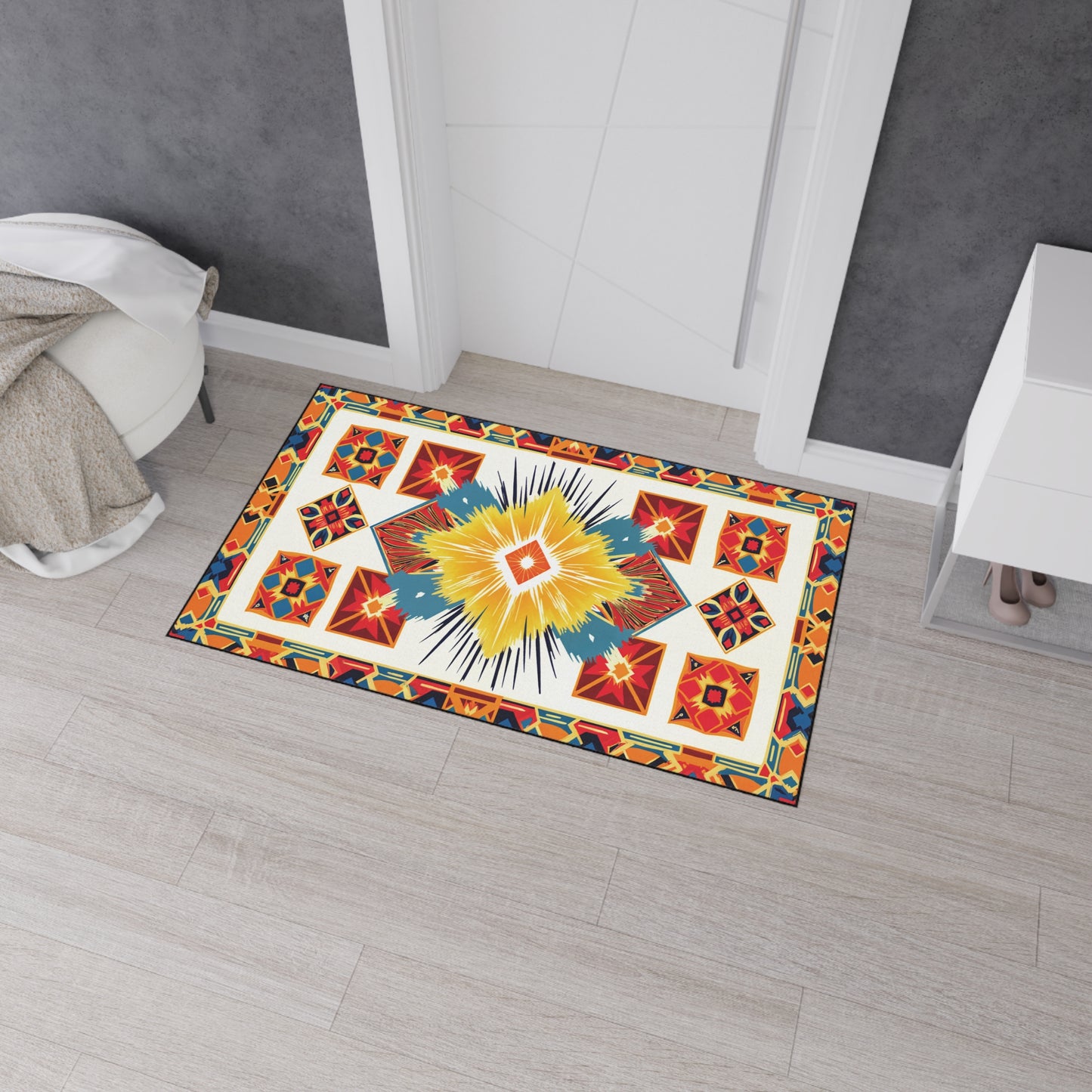 A rectangular rug with a vibrant geometric pattern, inspired by African-inspired floor mats, features yellow, red, blue, and black shapes. It lies on light wood flooring in front of a white door with a beige blanket draped nearby.