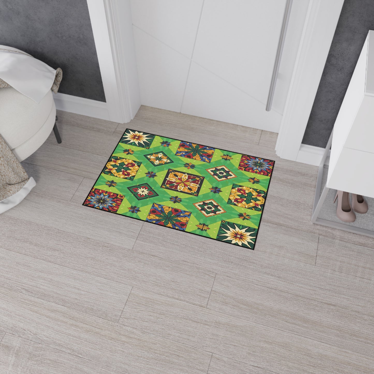 A colorful rectangular rug with African-inspired aesthetics and geometric floral patterns in red, yellow, green, and blue sits on a light wood floor by a white door. The modern setting includes a white round chair, cabinet, and beige heels.