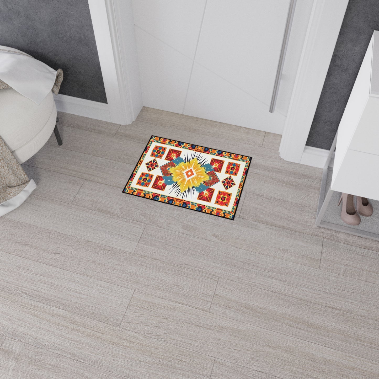 A small, rectangular doormat with a colorful geometric and floral pattern in red, yellow, blue, and orange lies on light wood flooring near a white door. Its non-slip rubber backing keeps it secure—an ideal touch for African-inspired home decor.