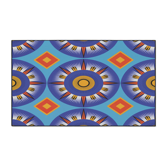 A rectangular African-inspired floor mat featuring bold geometric patterns in blue, orange, yellow, and white. Large sunburst circles alternate with orange diamonds on a bright blue background. Includes a non-slip rubber backing for safety.