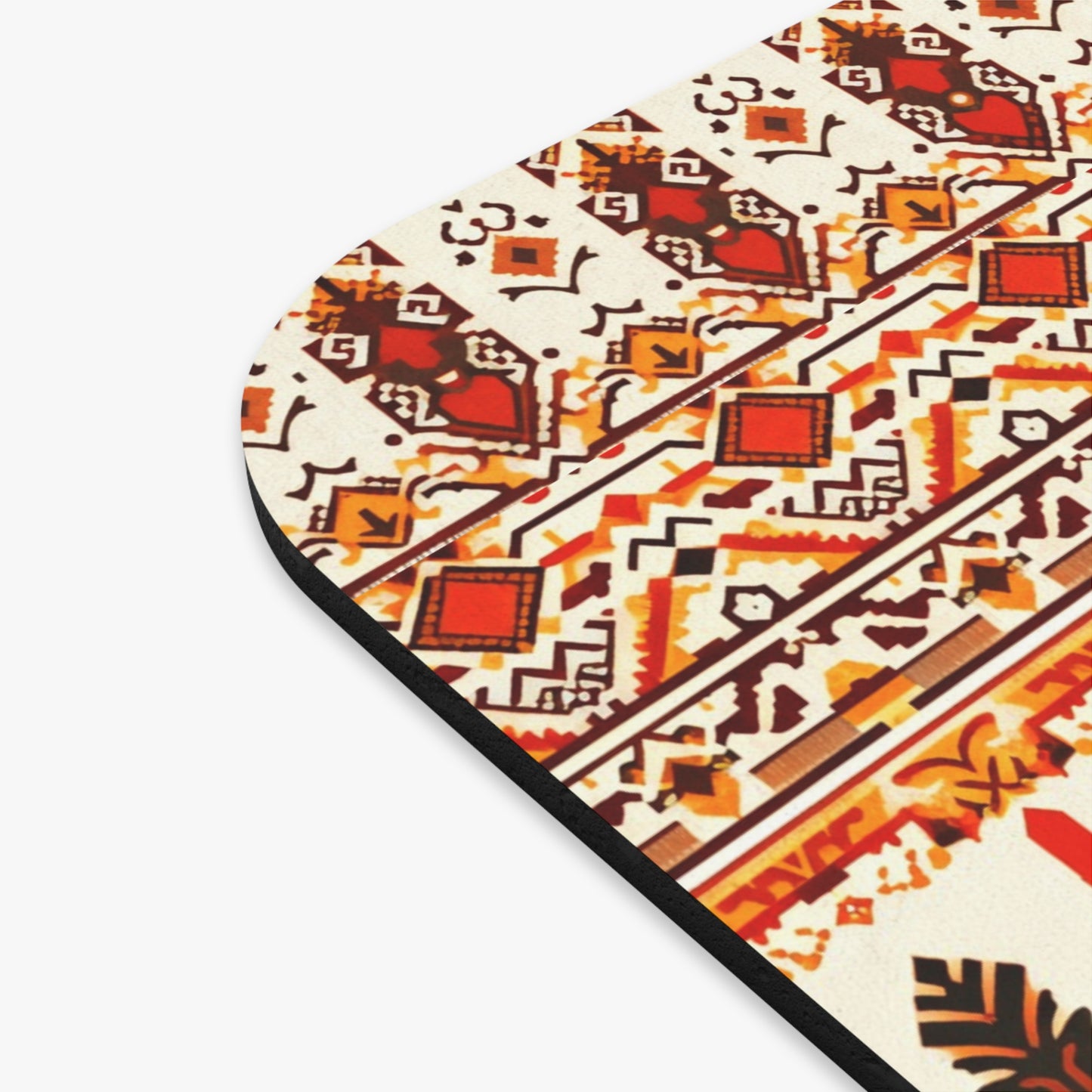 Close-up of a rounded corner of an African-inspired mouse pad featuring a geometric, tribal-inspired pattern in red, orange, brown, and black on cream. Includes diamonds, arrows, and abstract shapes in horizontal bands with a non-slip rubber base.
