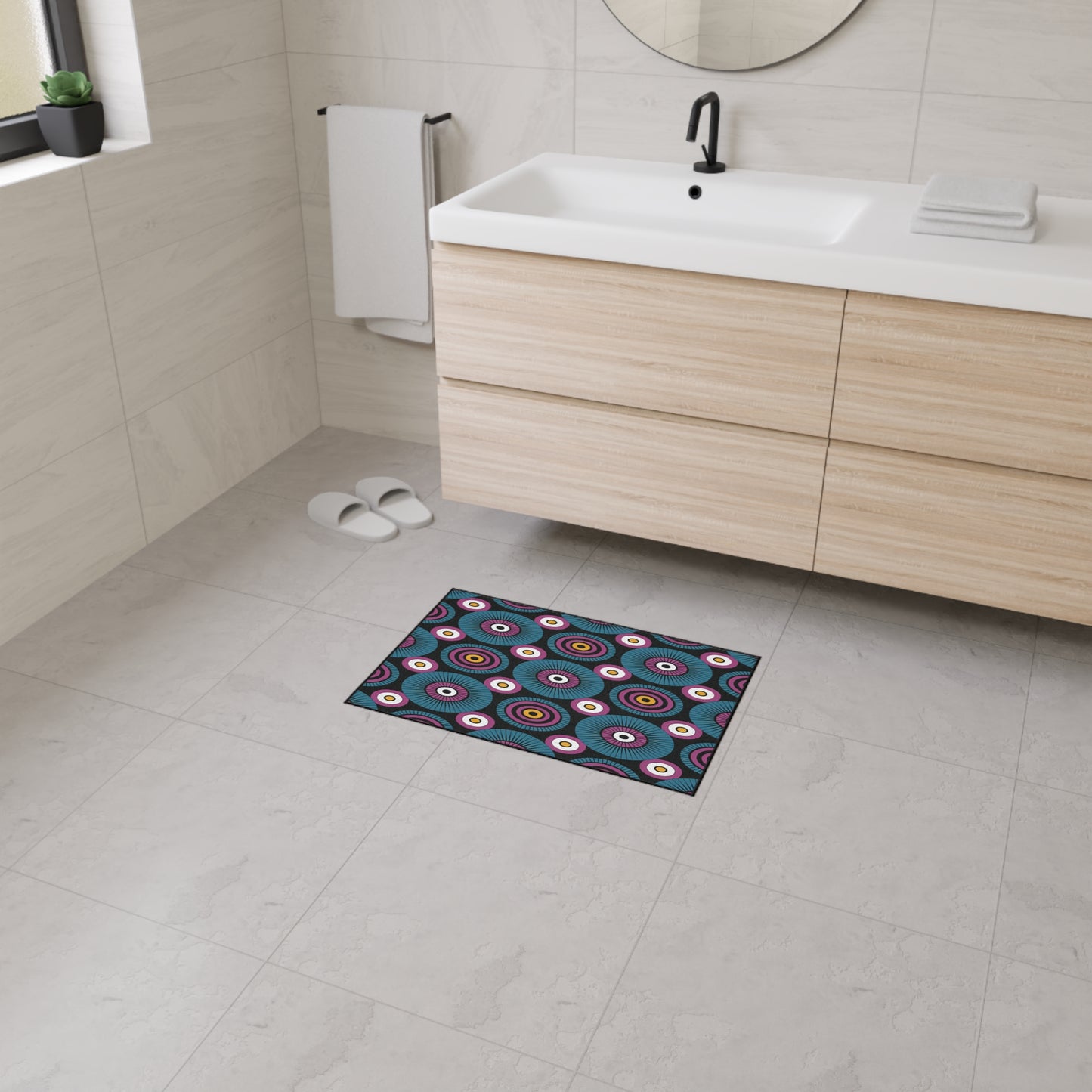 Modern bathroom with light gray tile floor and walls, floating wooden vanity with white sink, black faucet, round mirror, folded towels, a towel on a wall rack, white slippers, and an African-inspired custom floor mat with geometric circular patterns and non-slip rubber backing.