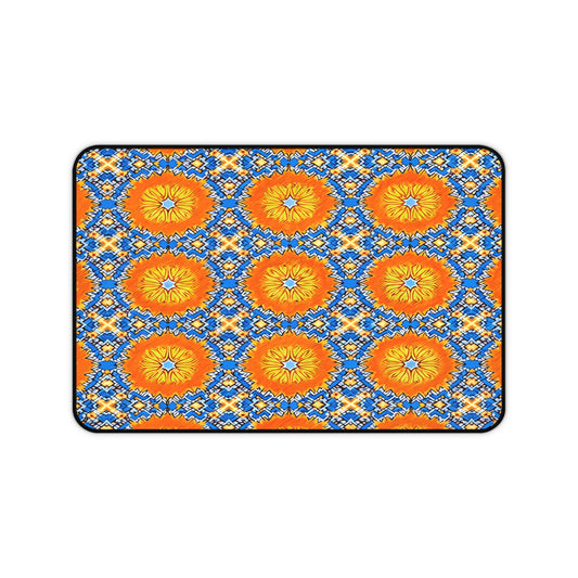 A rectangular neoprene desk mat with a vibrant geometric pattern features large orange and yellow circular shapes on a blue and white zigzag background, bordered by a thin black outline. This ergonomic desk mat is a colorful workspace accessory.