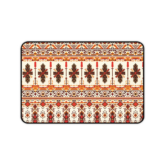 A rectangular neoprene desk mat features a symmetrical, intricate folk-inspired pattern in red, orange, brown, and yellow on a cream background, with repeating rows of stylized leaves and geometric shapes, bordered by a thin black outline.