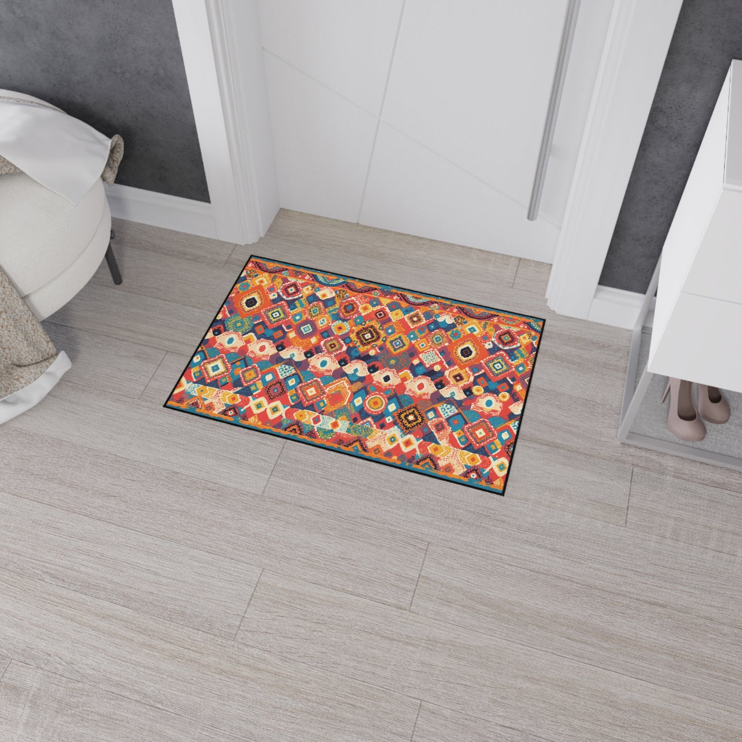 A rectangular doormat with a vibrant geometric pattern in red, orange, blue, and yellow adds African-inspired aesthetics to the room. Its non-slip rubber backing keeps it secure on the light wood floor by a white door amid modern decor.