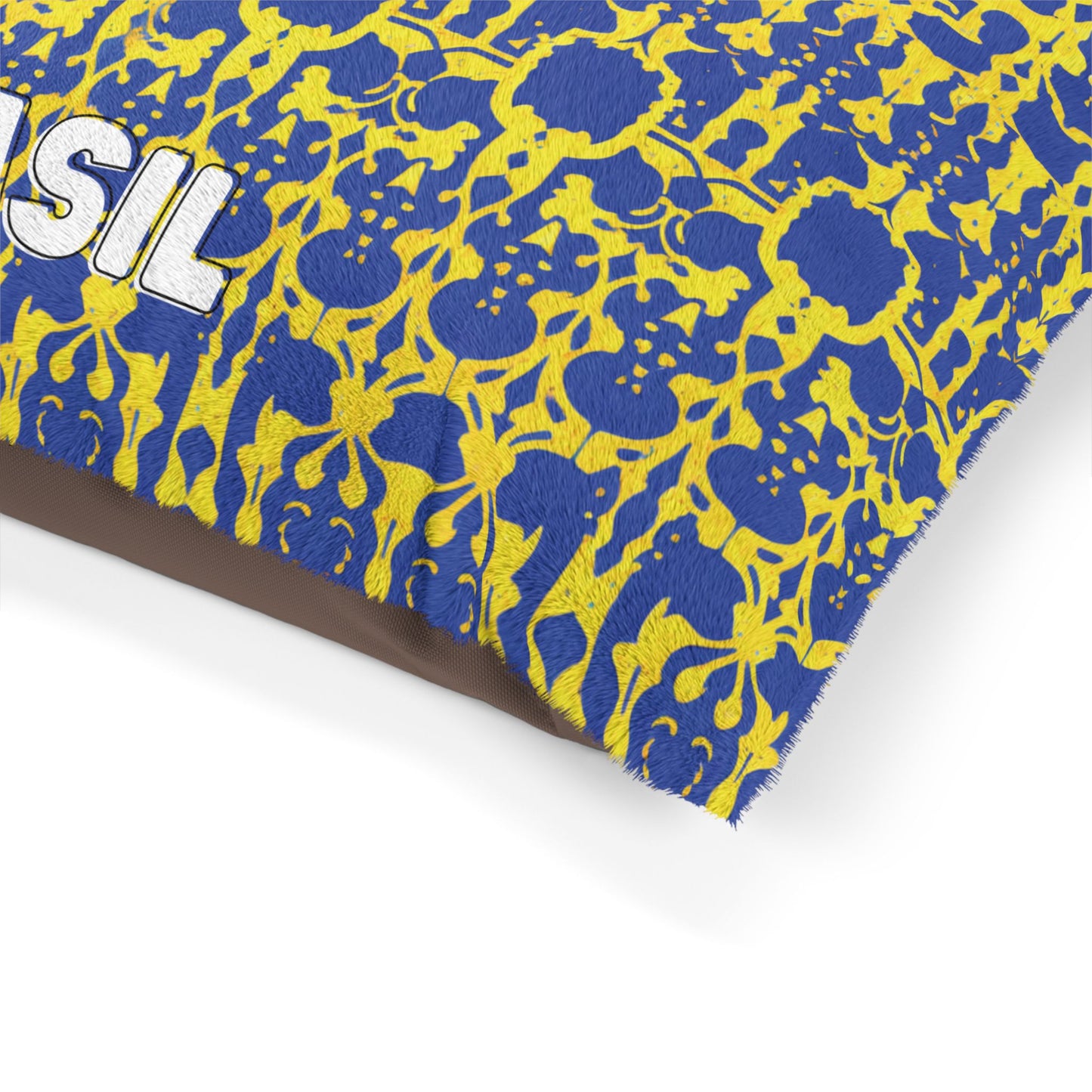 A close-up of a blue fabric pillow with a yellow, African-Inspired floral and vine pattern. The partial word SIL in bold white letters is visible on the left side. The fabric has a textured, soft appearance, and the pillow edges are slightly frayed.