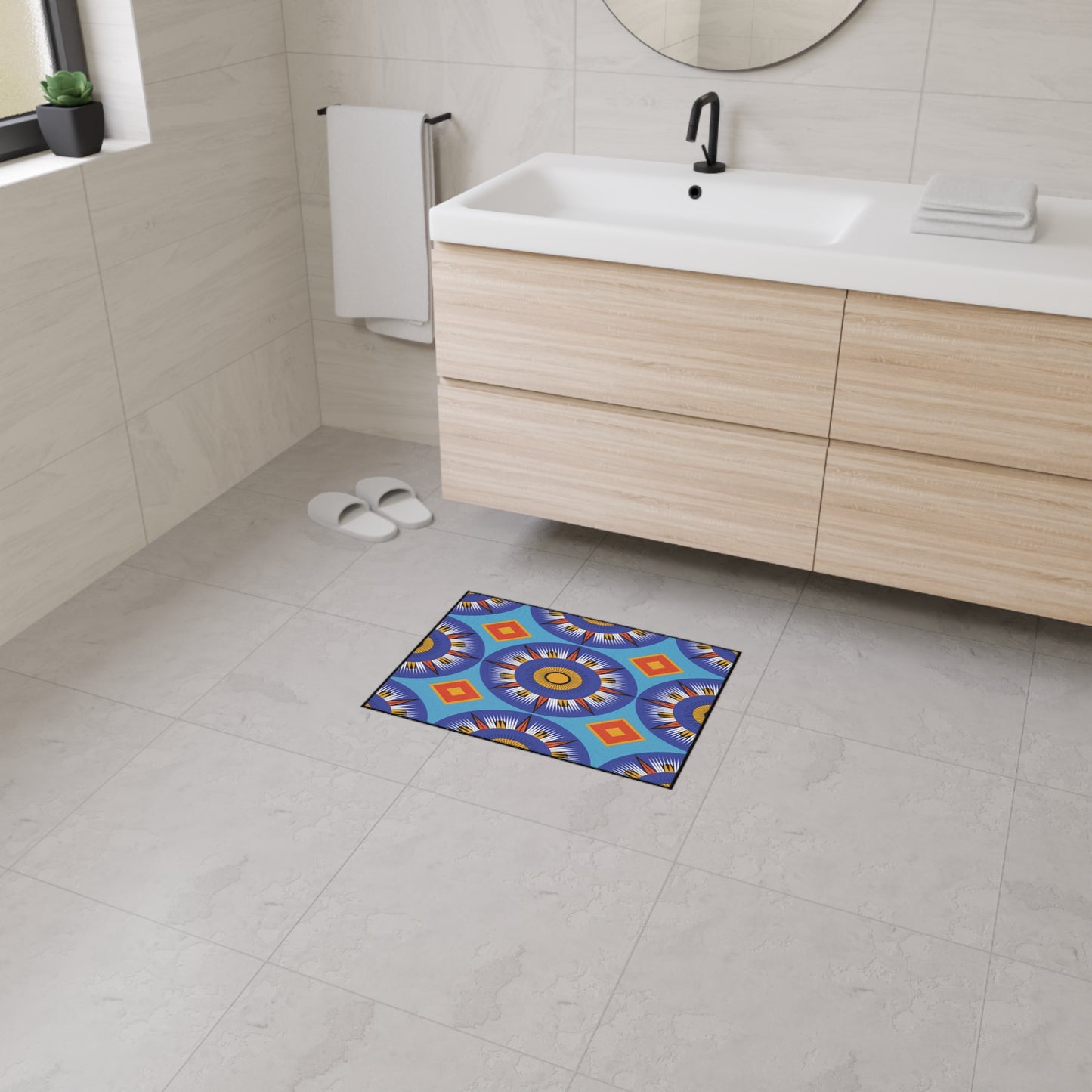 A modern bathroom with light tiled floors, a wooden vanity with a sink and towels, and white slippers by the wall. An African-inspired, geometric-patterned custom floor mat adds color and is non-slip for safety in front of the vanity.