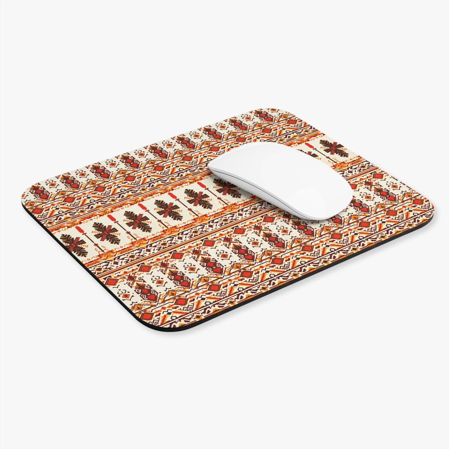 A white wireless mouse sits on an African-inspired mouse pad adorned with intricate, symmetrical patterns in red, orange, and beige—a vibrant workspace decor piece. The non-slip desk accessory rests against a plain white background.