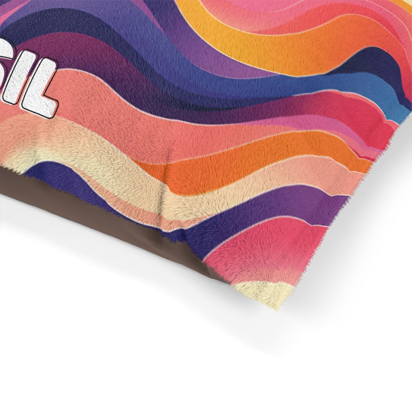 A close-up of a pillow corner featuring African-inspired colorful wavy stripes in pink, orange, purple, red, and cream. The surface has a soft, fuzzy texture. Part of white text with a dark outline is visible on the left side against a white background.