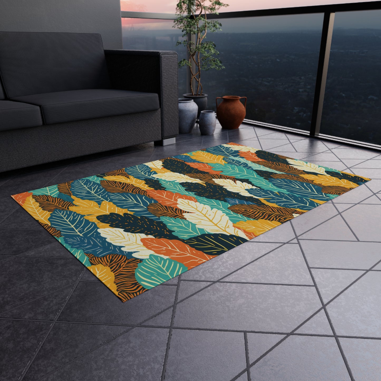 A colorful, African-inspired rug with a bold leaf pattern in teal, orange, mustard, green, and black sits on a tiled balcony floor. Nearby are a gray sofa, potted plants, and a railing overlooking a cityscape at sunset.