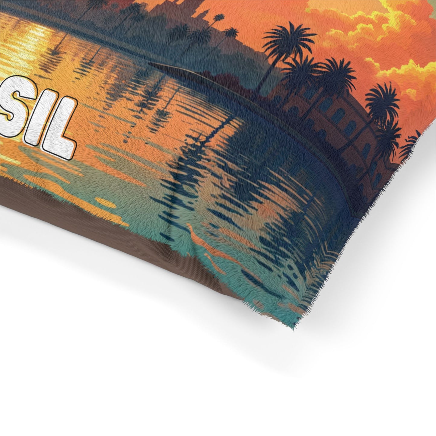 A close-up of a pillow corner featuring a vibrant sunset scene with palm trees and buildings reflected on water. The sky is orange and yellow. Durable construction ensures lasting quality, while part of the white text SIL is visible on the fabric.