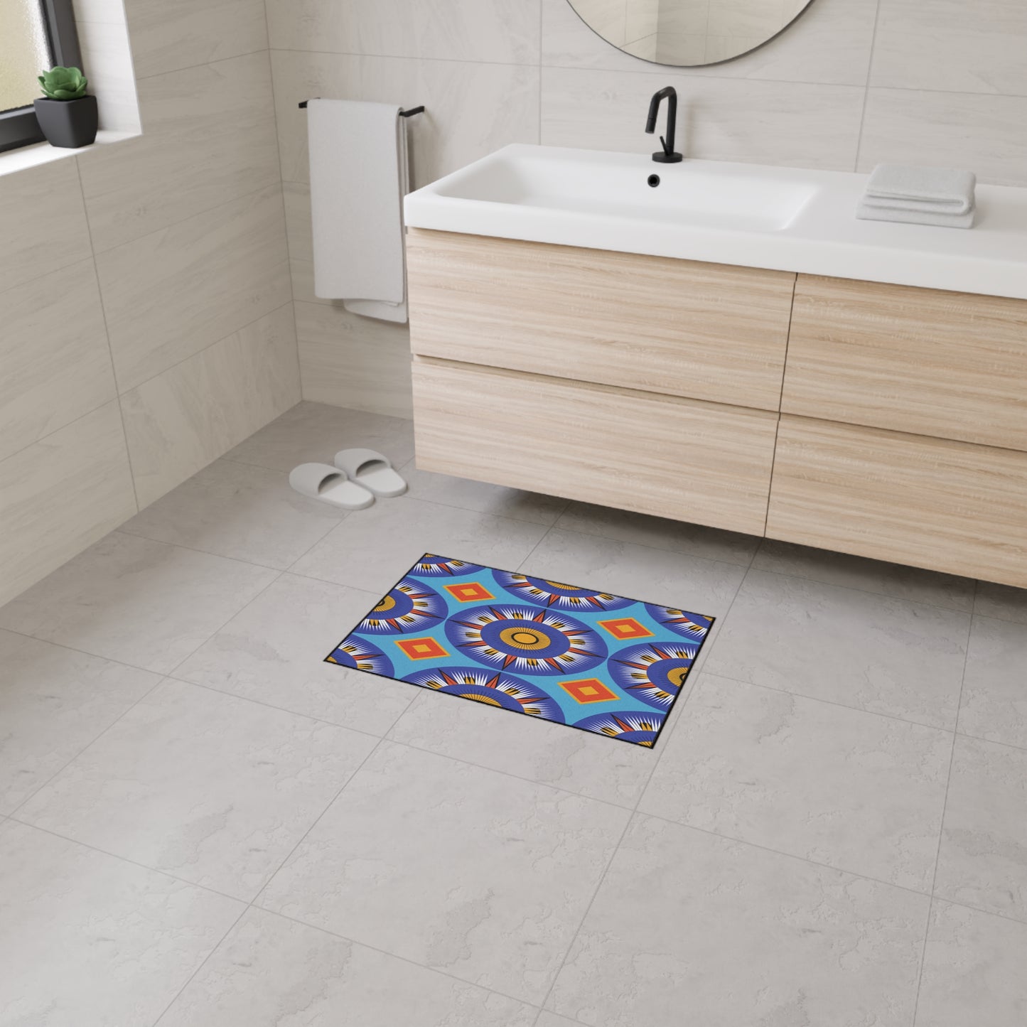 Modern bathroom with light wood vanity, white sink, round mirror, towel, and slippers. A colorful rectangular bath mat featuring African-inspired aesthetics and non-slip rubber backing brightens the light gray tiled floor near the window-lit sink.
