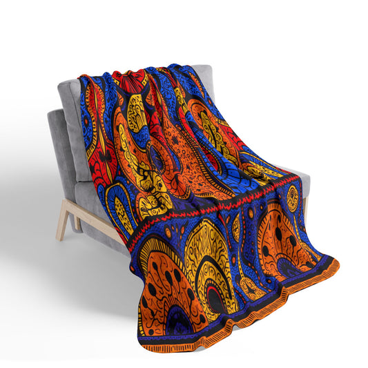 A gray, modern-style chair is draped with a vibrant, African-inspired blanket. The bold abstract designs in red, blue, yellow, and orange with black accents create a lively contrast against the neutral chair and white background.