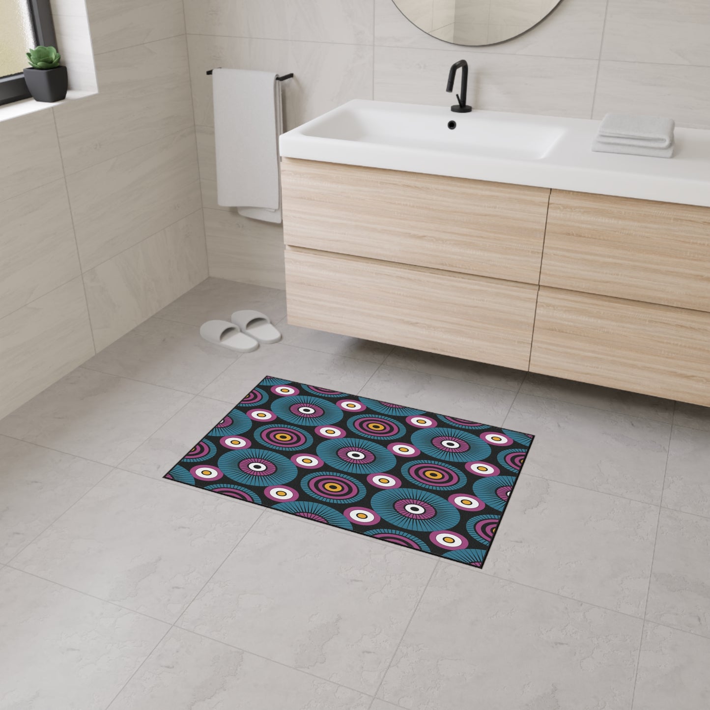 A modern bathroom with light beige tiles, a floating wood vanity, white sink, round mirror, and black faucet. The floor features an African-inspired non-slip rug with concentric circles and geometric patterns in bold colors.