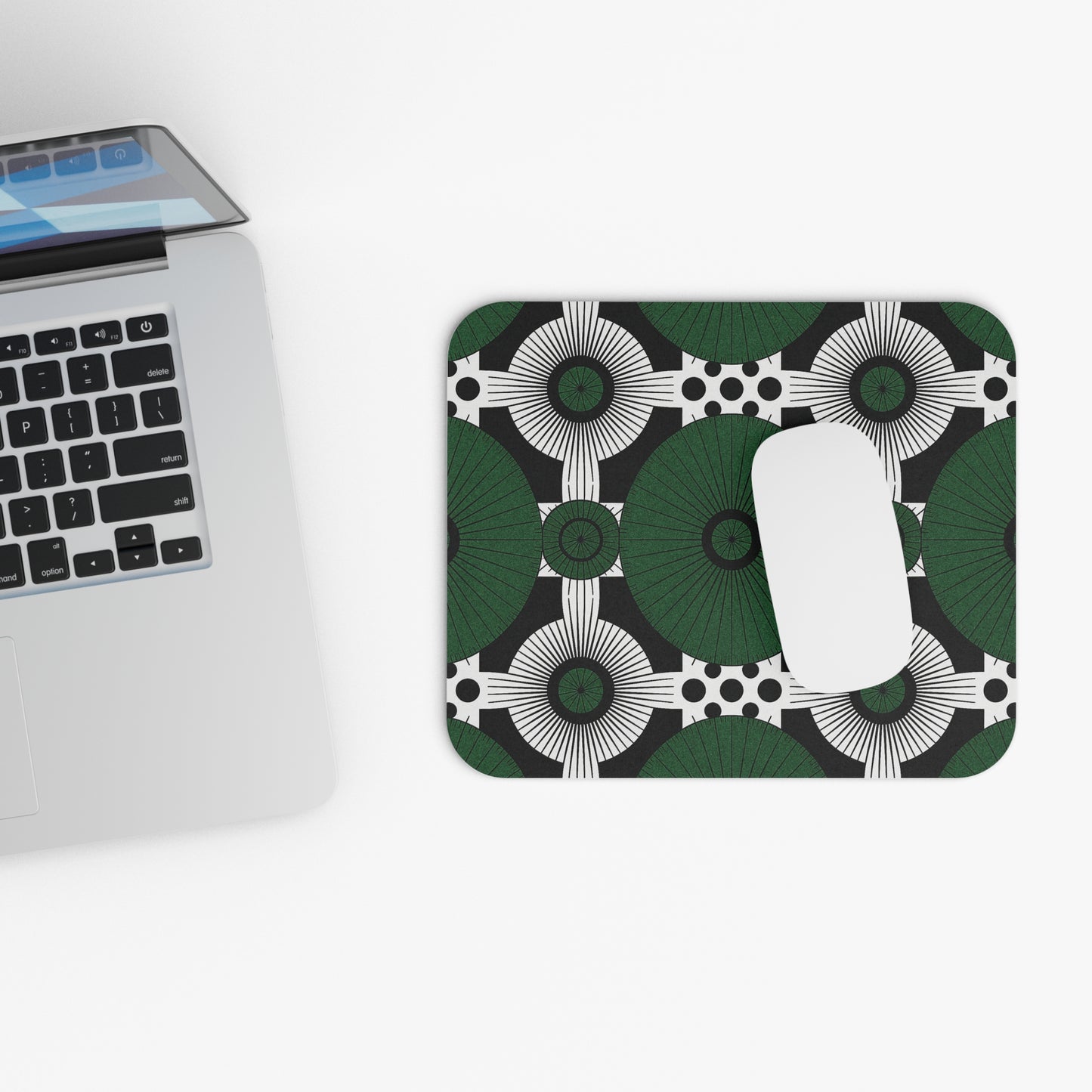 A silver laptop sits on a white surface next to an African-inspired mouse pad featuring green, black, and white circles. This non-slip desk accessory boasts durable high-density foam, with a white wireless mouse resting on top.