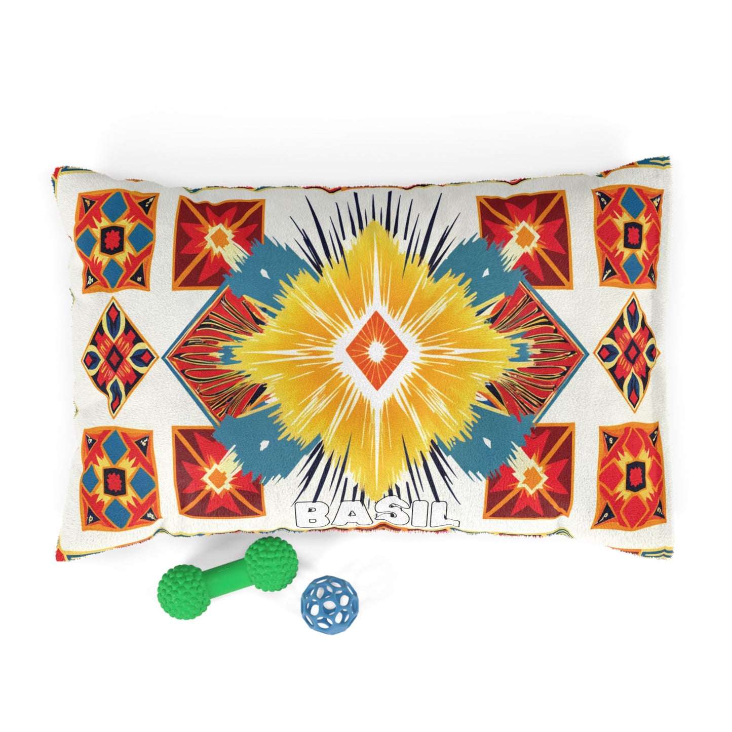 A colorful, rectangular pillow with African-inspired geometric patterns in yellow, red, teal, and orange sits on a white background. BASIL is printed in bold white letters at the bottom center. Two textured dog toys, one green and one blue, are nearby.