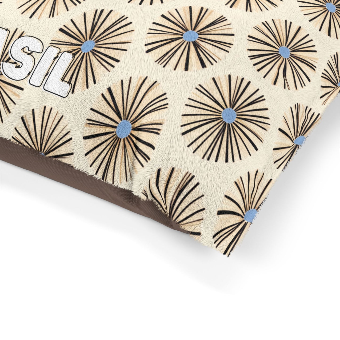 A close-up of a beige fabric with an African-inspired pattern of large, round, starburst shapes in black and tan, each featuring a blue dot in the center. Part of the word “BASIL” is visible on the fabric against a plain white background.