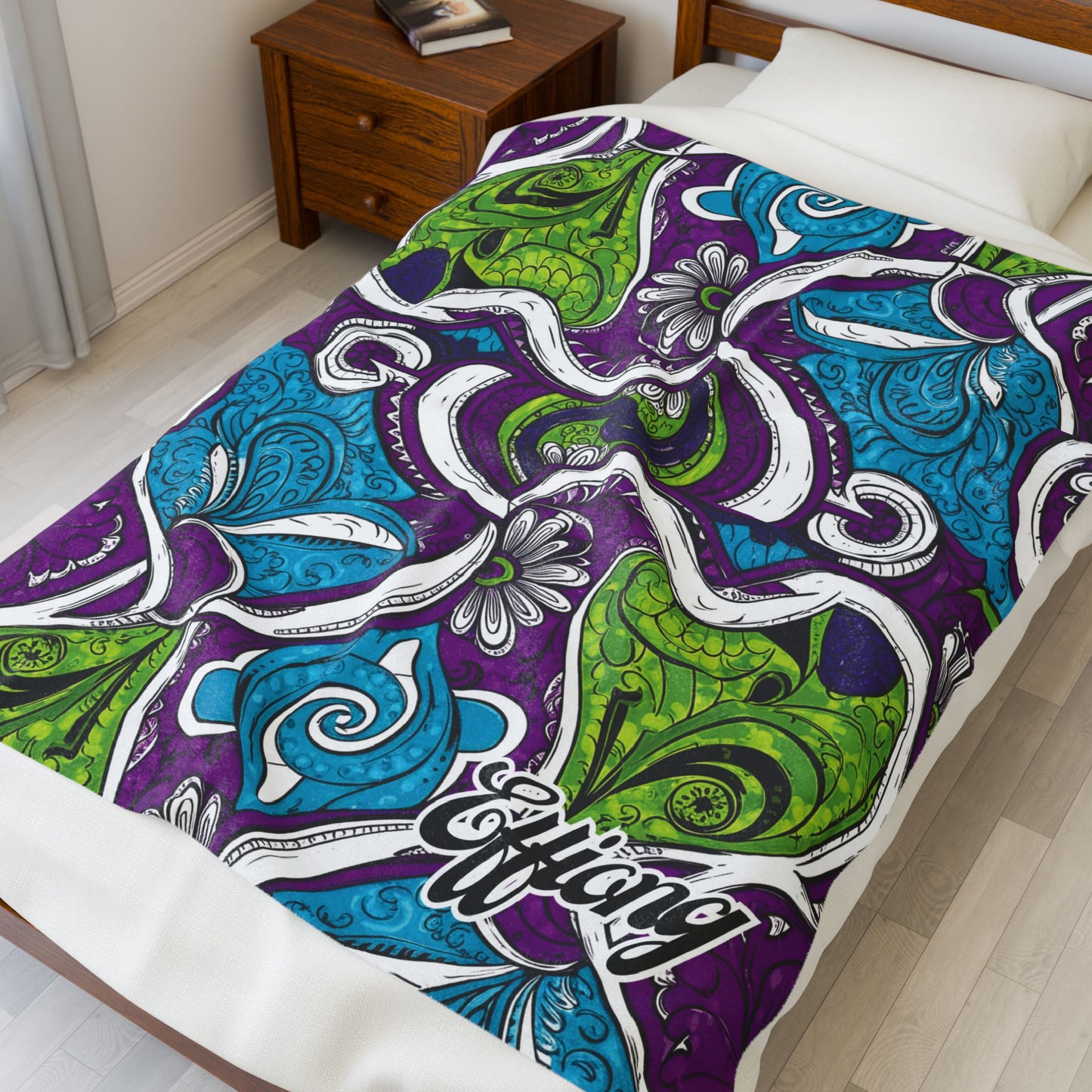 A neatly made bed features an African-inspired blanket with swirling, abstract patterns in purple, blue, and green. The word Effiang is written in stylized script on the corner. A wooden nightstand and lamp are nearby.
