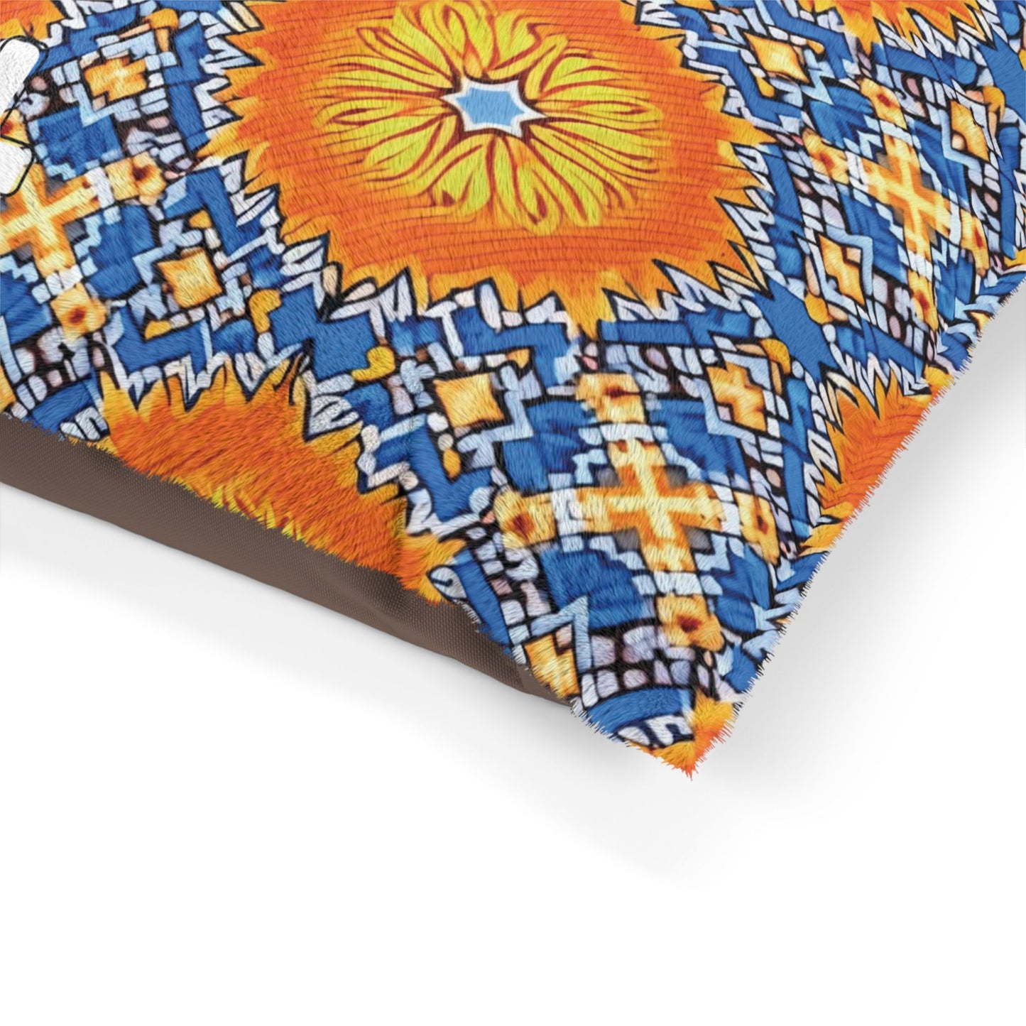 Close-up of a cozy pet pillow with a colorful geometric pattern. The design features a large orange sunburst surrounded by blue, yellow, and white diamond shapes, creating a vivid mosaic on textured fabric. The pillow rests on a white background.