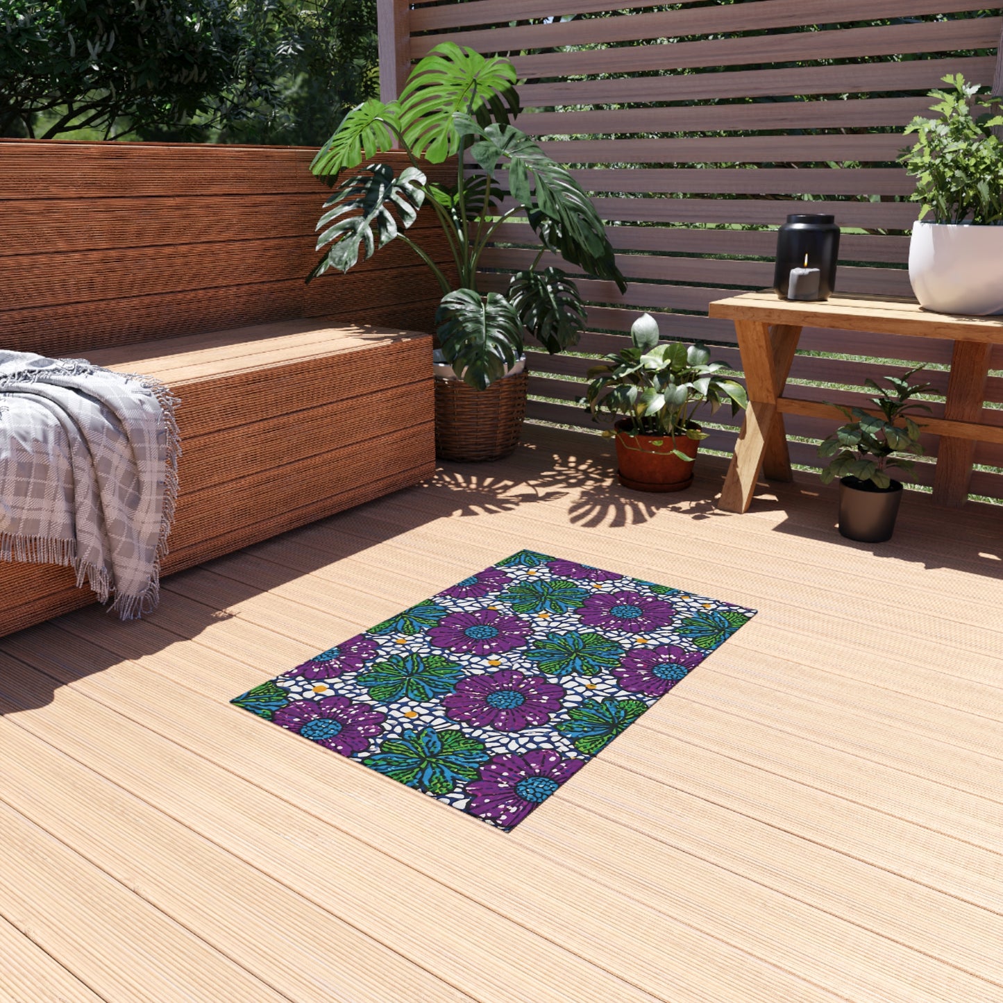 A cozy wooden patio features a bench with a gray plaid throw, several potted plants, and a bright African outdoor rug with bold purple, blue, and green geometric floral patterns. Sunlight streams in, creating a peaceful atmosphere.