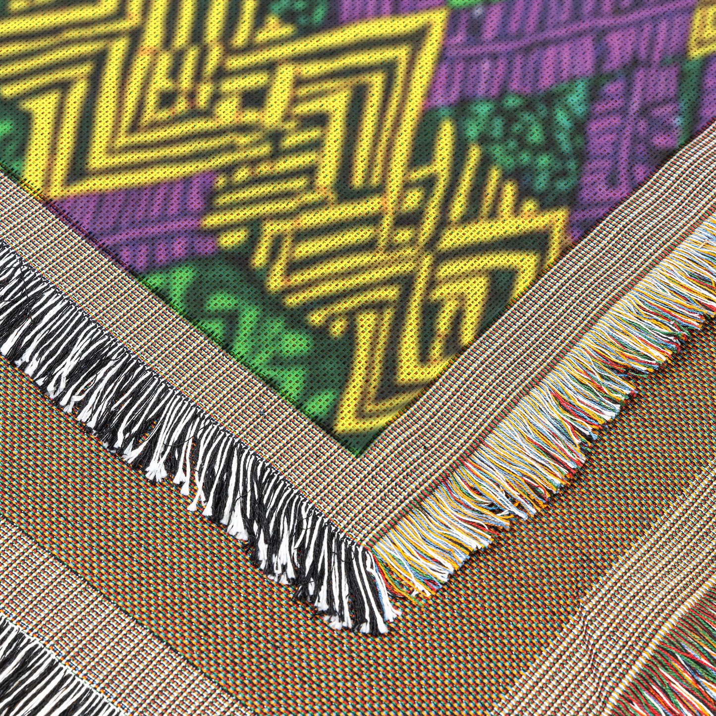 Close-up of a vibrant throw blanket featuring geometric yellow, green, and purple West African print patterns. Two beige fringed edges with multicolored threads highlight the fabric’s bold texture and decorative borders.