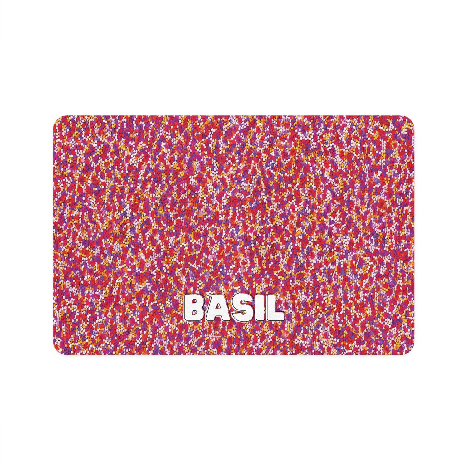 A rectangular mat with a dense, colorful confetti pattern in red, pink, yellow, and white. The word BASIL appears in bold white letters near the bottom center on a white background.