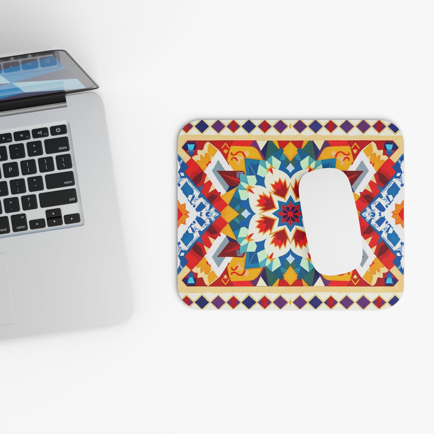 A laptop sits on a white surface next to a colorful rectangular mousepad with a bold geometric pattern and a white mouse placed on top of it.