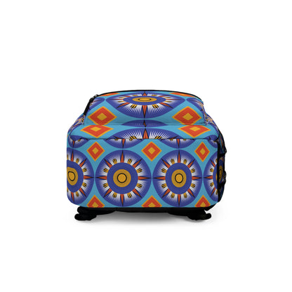 A colorful ottoman with a vibrant geometric pattern in blue, yellow, orange, and red. Reminiscent of a boho chic rucksack, its circular sunburst shapes and diamond motifs create a bold, artistic look. The ottoman has short black legs and a soft fabric texture.