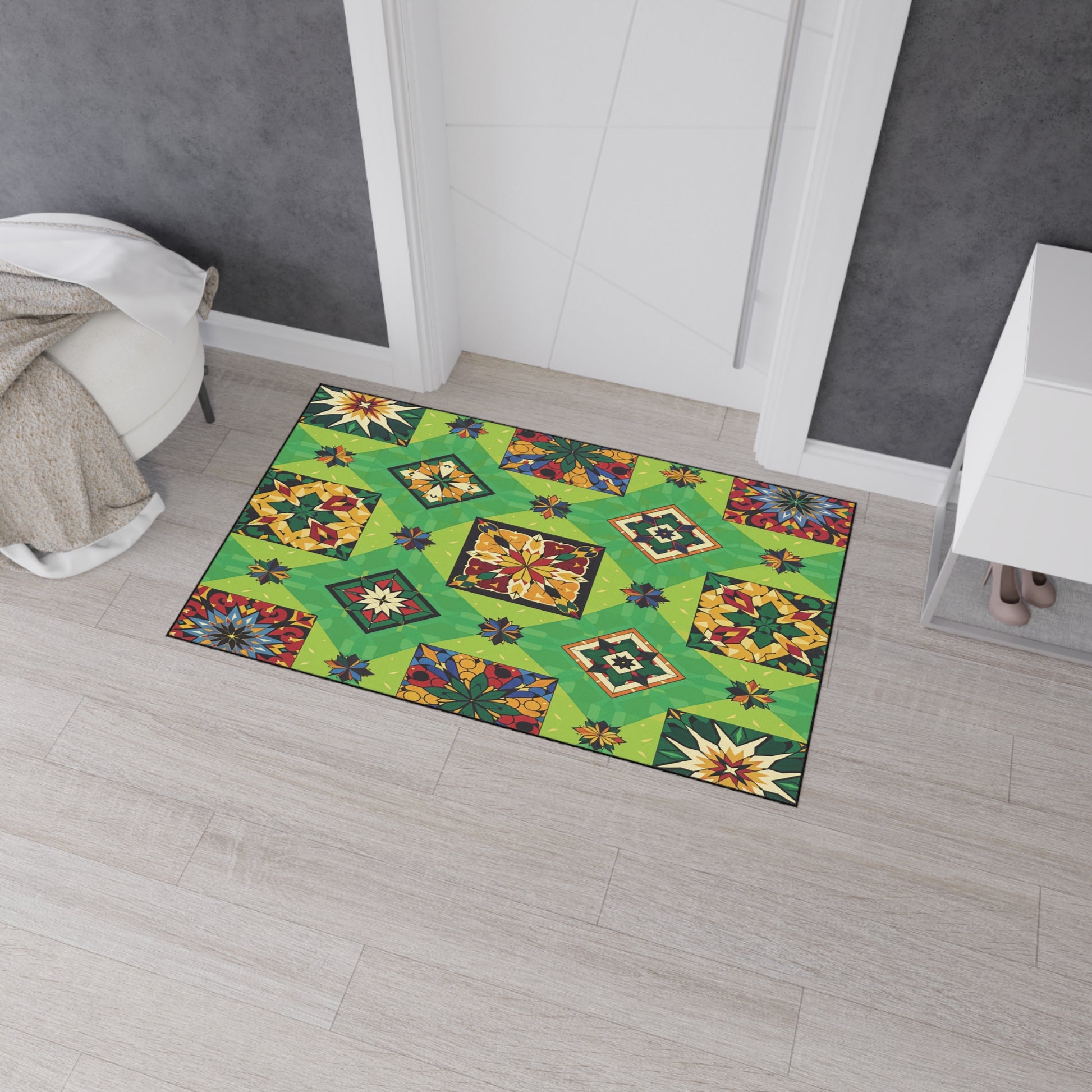 A colorful rectangular rug with a green geometric patchwork pattern, floral motifs, and African-inspired aesthetics lies on light wood flooring in front of a white door, near a gray wall, a white dresser, and a beige throw blanket draped over a chair.
