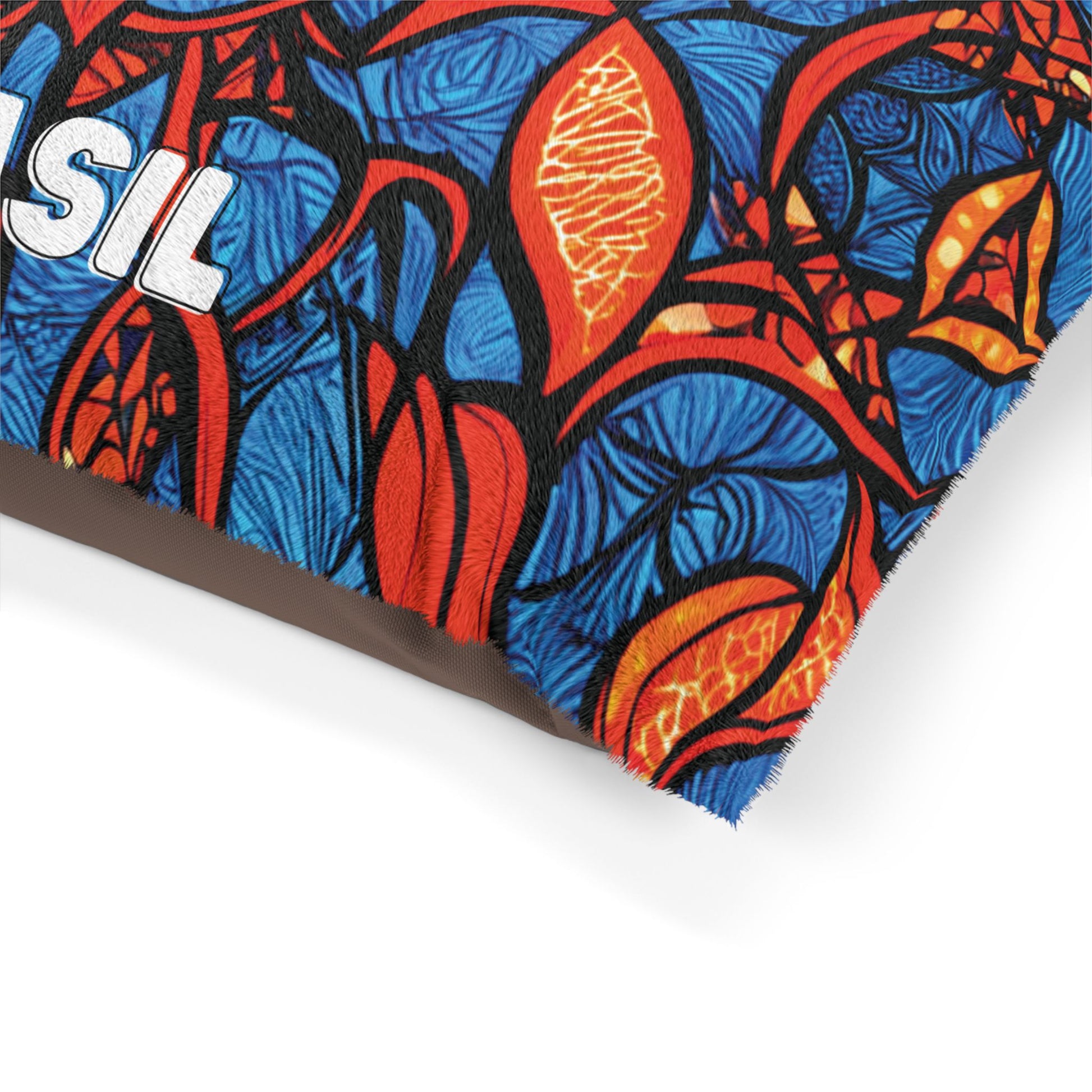 A close-up of a fabric with a colorful, bold pattern of red, orange, and blue abstract leaves and shapes. BRASIL is partly visible in white letters on the upper left. The fabric appears to be part of a stylish pet bed or cushion.